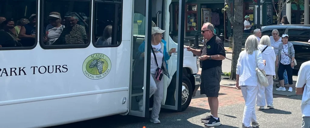 A guide steadying a guest as she steps down from the enclosed Classic Tour bus in downtown Bar Harbor