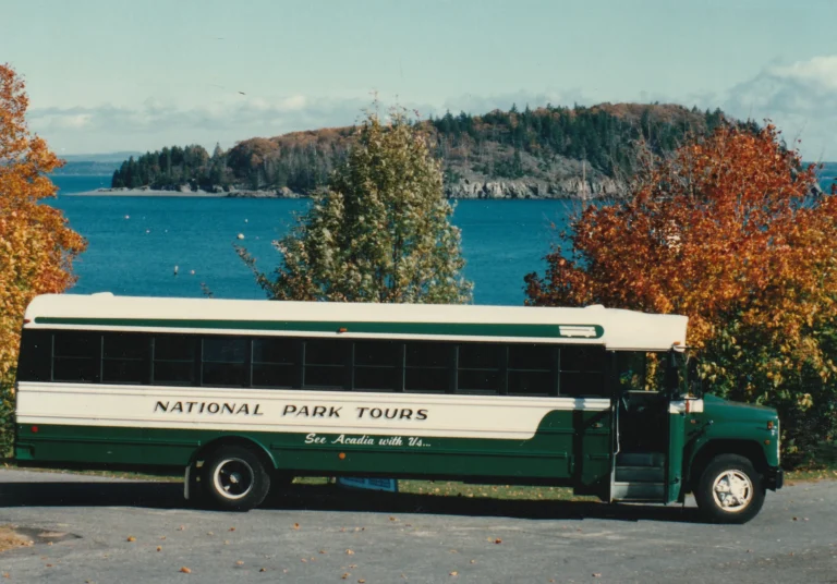 The green and white National Park Tours coach of the 1980s parked along the Acadia shoreline in autumn