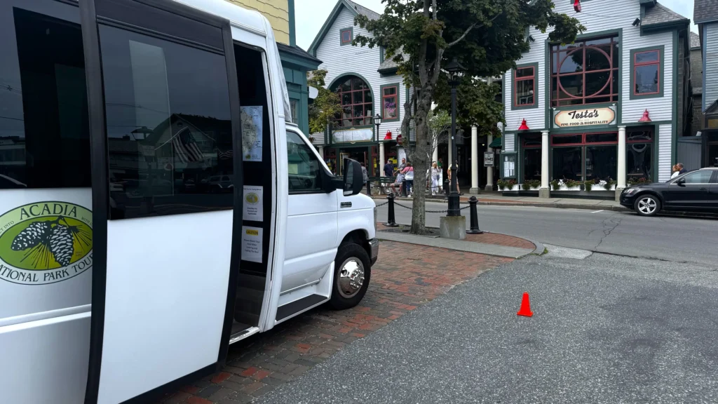 An Acadia National Park Tours bus with its door open for boarding on Main Street, Bar Harbor