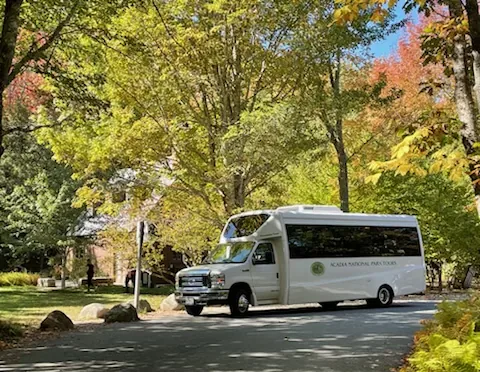 An Acadia National Park Tours coach parked on a quiet road beneath autumn foliage