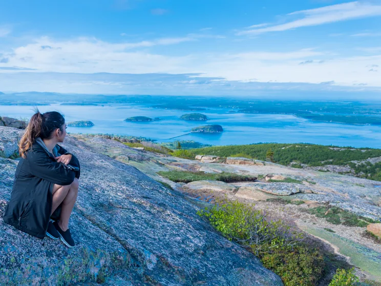 A visitor on the granite summit of Cadillac Mountain looking out over Frenchman Bay and the islands