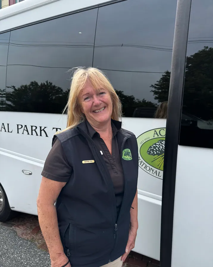 Guide Heather Rice smiling beside the Acadia National Park Tours coach in Bar Harbor