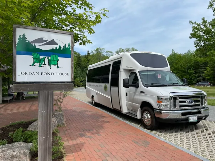 The carved Jordan Pond House sign with an Acadia National Park Tours coach on the drive behind it