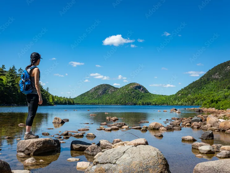 A walker at the edge of Jordan Pond looking across the clear water to the Bubbles