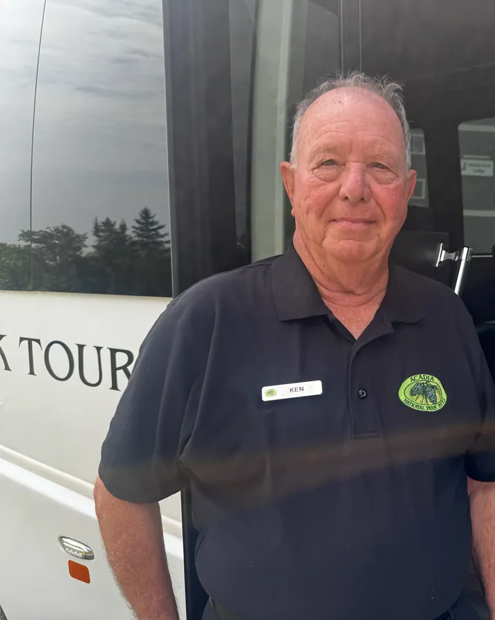 Guide Ken Cassels in a branded Acadia National Park Tours polo beside the tour coach