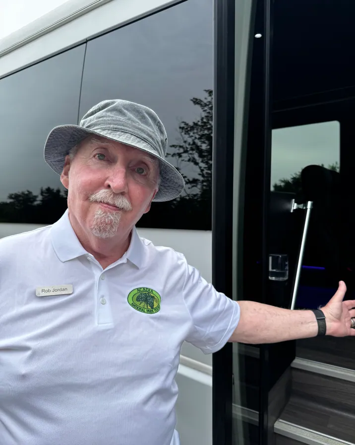 Guide Rob Jordan in a flat cap waving beside the Acadia National Park Tours coach