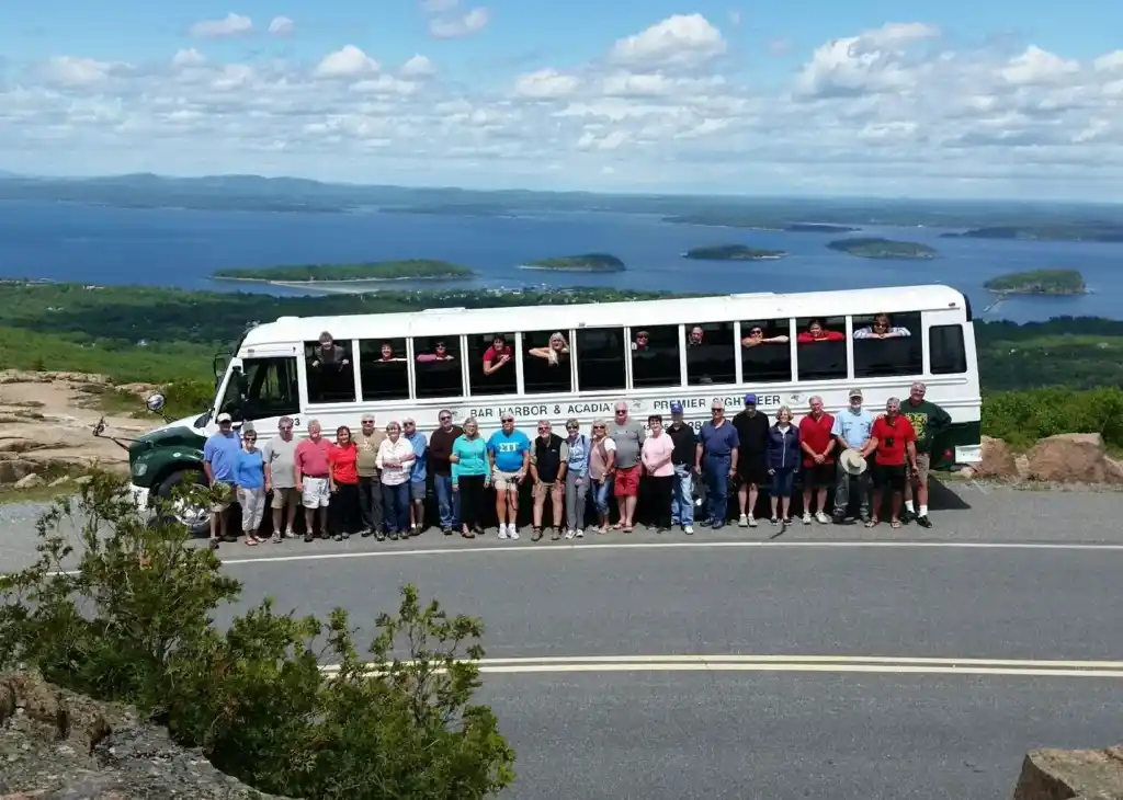 A tour group posed with their coach at an Acadia overlook above Frenchman Bay and the islands